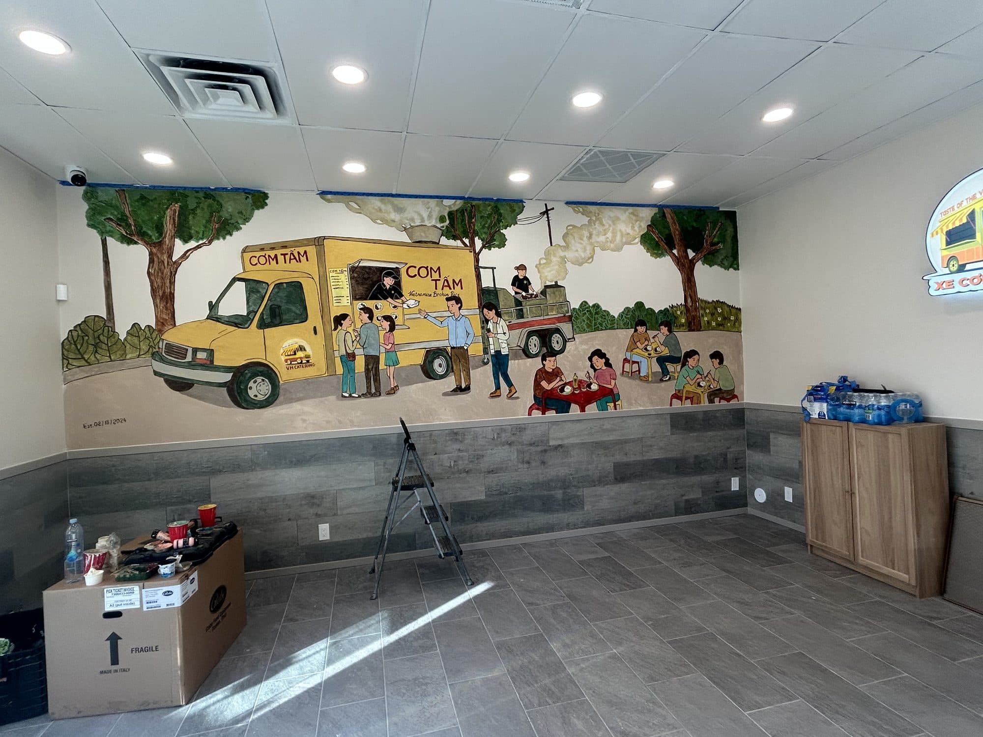 Hand-painted mural of a yellow cơm tấm food truck and customers across a restaurant wall