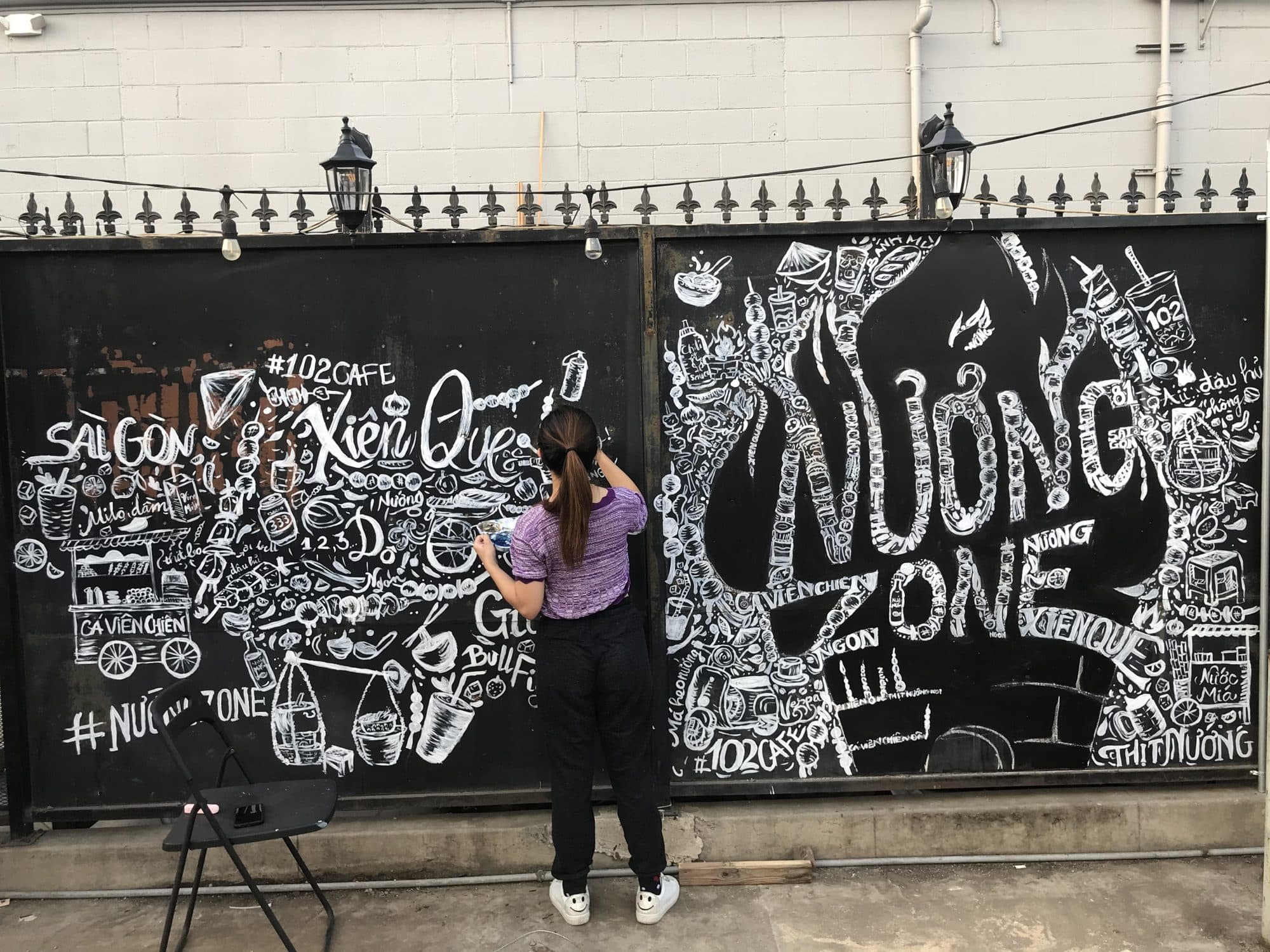 Eve hand-lettering a black and white chalk-style wall for Nướng Zone