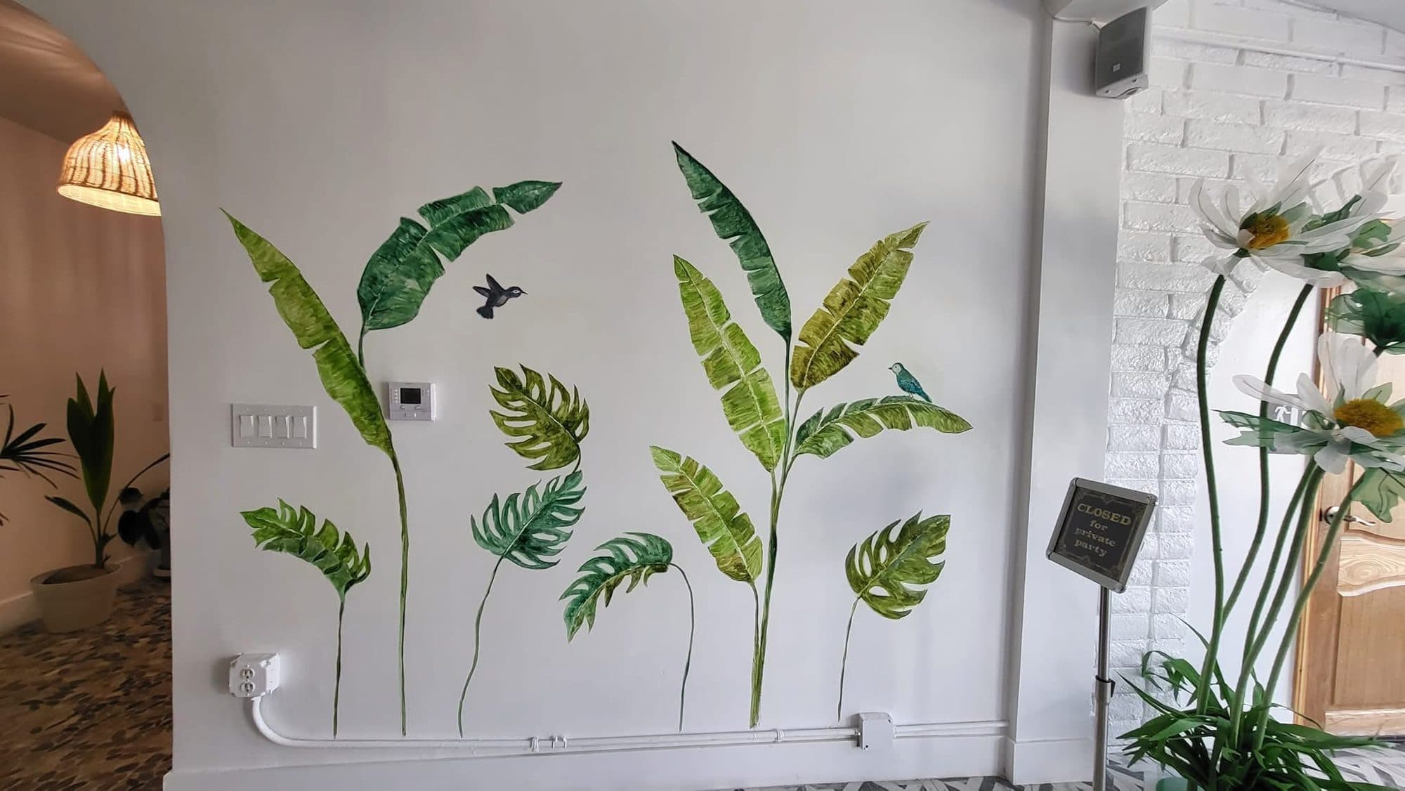 Painted banana and monstera leaves on a white café wall at The Vintage 1979 in Garden Grove
